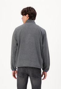 Gray fleece jacket with a high collar, relaxed fit, and ribbed cuffs. The hem is slightly curved. Visible blue accent at the cuffs.