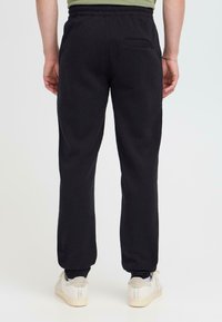 Zwarte sweatpants van zacht materiaal, met een elastische tailleband, smalle pasvorm en een klein achterzakje. Accentueert met witte sneakers.