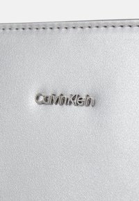 Srebrny portfel z sztucznej skóry z fakturowanym wykończeniem i wyraźnym logo "Calvin Klein". Szyte krawędzie zwiększają trwałość.