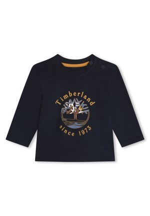 Pitkät hihat tummansininen paita, joka on valmistettu puuvillasta. Siinä on kultainen pyöreä Timberland-logo, jossa on kuvan puusta, ja tekstinä "since 1973" alla.