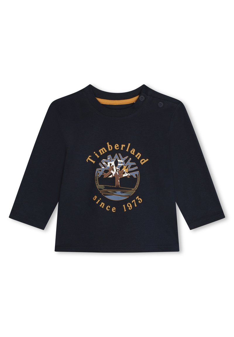 Pitkät hihat tummansininen paita, joka on valmistettu puuvillasta. Siinä on kultainen pyöreä Timberland-logo, jossa on kuvan puusta, ja tekstinä "since 1973" alla.