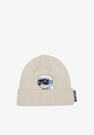 Bonnet en tricot beige clair avec bord replié et visage de dessin animé brodé portant des lunettes de ski et un foulard blanc.