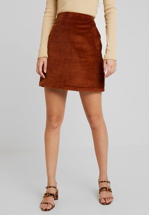 Femme portant une mini-jupe en velours côtelé marron, un haut beige à manches longues et des sandales ouvertes à talons blocs imprimé léopard.