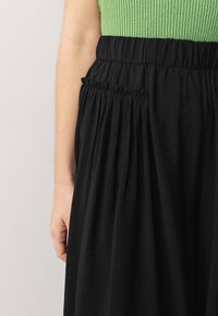 Svart plisserad kjol med elastiskt midjeband, kombinerad med en grön ribbad topp. Tyget verkar vara lätt och texturerat.