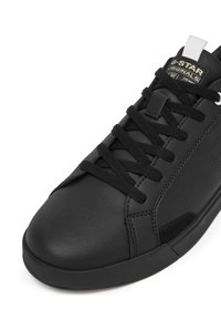 Melnie augstāki sporta apavi ar gludu ādas augšdaļu, apaļu purngalu, melnām auklām un baltu izvelkamu cilpu. Iekļauti zīmola nosaukums uz mēles un perforācijas.