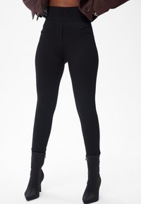 Czarne legginsy wykonane z elastycznego materiału, z wysokim stanem i subtelnymi kieszeniami z przodu. Połączone z czarnymi, szpiczastymi botkami sięgającymi do kostek.