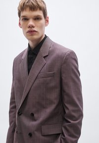 Doppelreihiger Blazer aus hellmauvefarbenem Stoff mit einer dezenten Textur. Mit schwarzen Knöpfen, einer Brusttasche und einem Revers mit Kerbe.