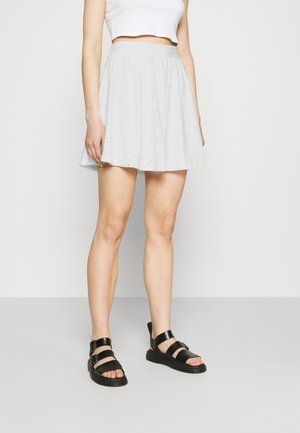 Ljusgrå knä-length kjol gjord av mjukt tyg med ett texturerat mönster. I kombination med svarta sandaletter med remmar och en kort vit topp.