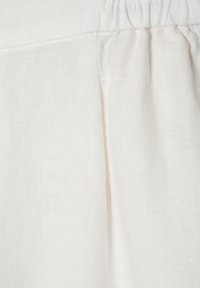 Light beige linen fabric with a slightly textured surface and gathered elastic waist. Features soft pleats for added detail.