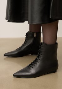 Mustad terava nina ja nööpidega ankle boots, kantud läbipaistvate mustade sukkade ja musta nahkse seeliku kombinatsiooniga.