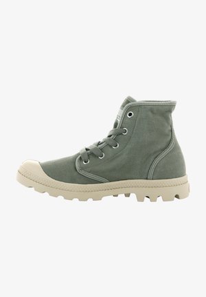 Bottines de cheville en toile verte avec un capuchon en caoutchouc et une semelle texturée blanche. Présente des œillets en métal et des détails de couture contrastants.