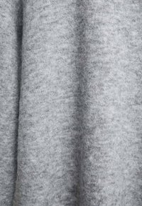 Tissu gris clair et doux avec une texture lisse. La surface présente de subtiles variations de ton, indiquant un design tricoté ou tissé.