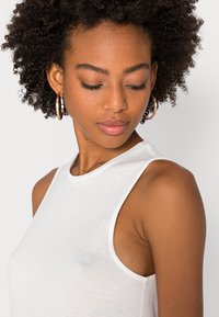 Top branco sem mangas com decote redondo, feito de material leve, com uma textura suave e linhas limpas.