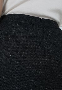 Jupe noire en tissu texturé avec un motif en chevrons. Elle présente une taille lisse et une fermeture éclair dissimulée à l'arrière.