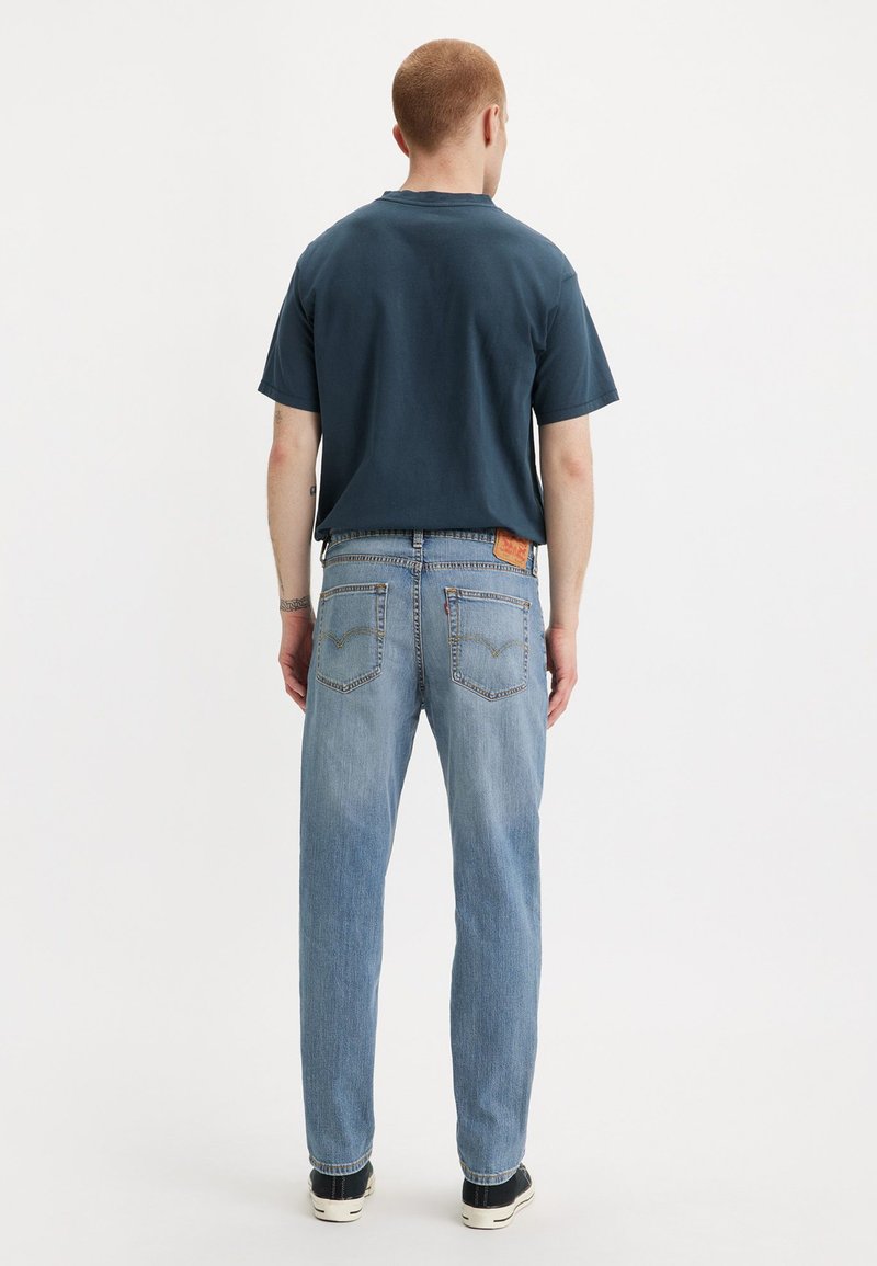 T-shirt en coton navy à manches courtes ; jeans straight-leg bleu clair avec patch au dos et deux poches arrière ; baskets noires.