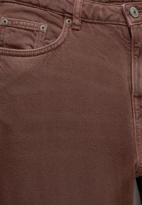 Jeans en denim marron texturé avec un design à cinq poches, comportant une fermeture éclair et un bouton en métal.