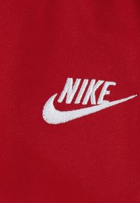 Tela roja con un logo bordado en blanco de "Nike", que incorpora un detalle distintivo de la marca Swoosh. Textura suave y color sólido.