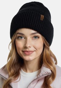 Czarna, prążkowana czapka beanie o teksturowanym wykończeniu z małą skórzaną metką. Zaprojektowana, aby ciasno przylegała, zapewniając ciepło i komfort.
