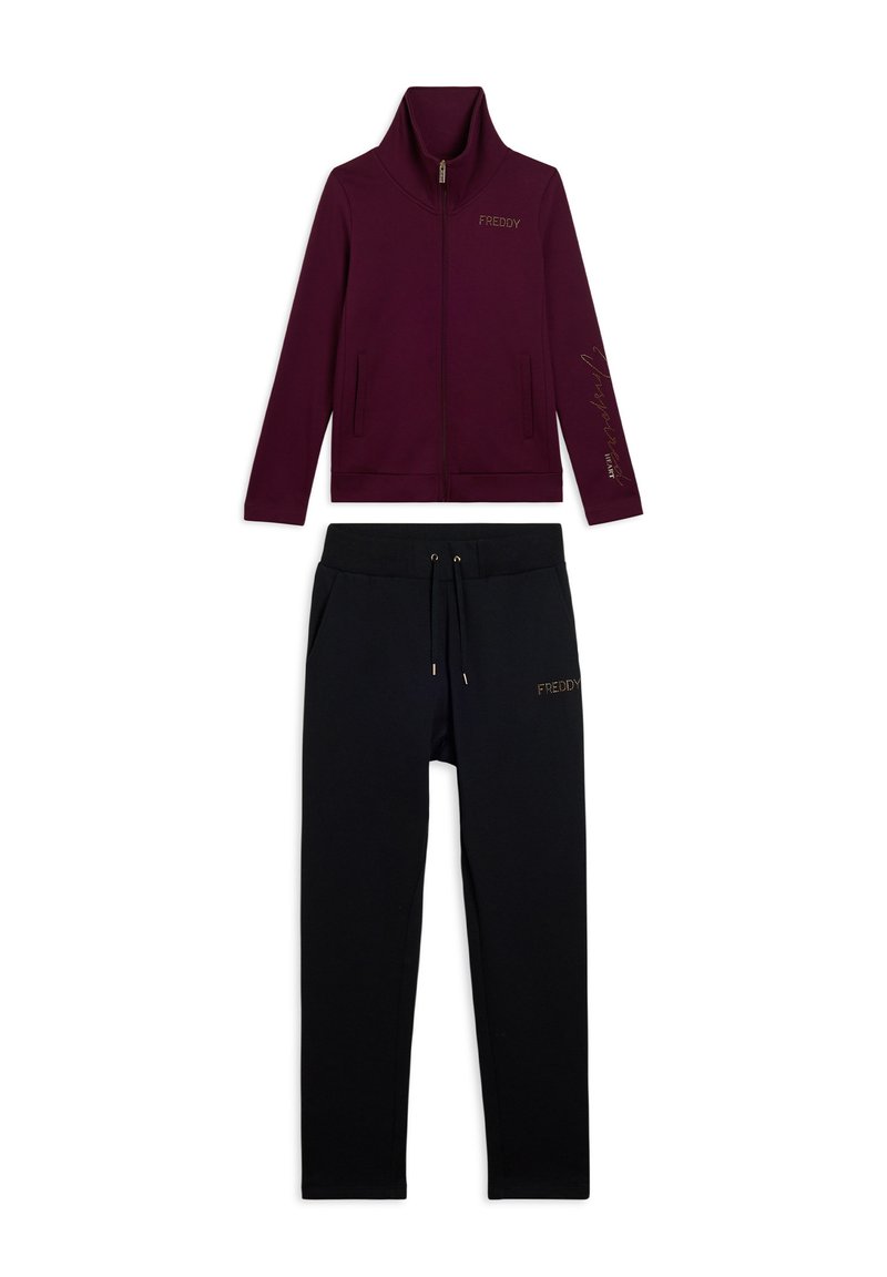 Giacca bordeaux con zip e colletto alto, abbinata a pantaloni neri con cordoncino, entrambi decorati con il logo "FREDDY" in lettere dorate.