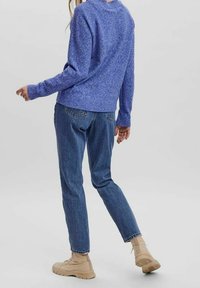 Blauer gestrickter Pullover mit strukturiertem Finish, kombiniert mit gerade geschnittenen dunkelblauen Jeans und beigen klobigen Sneakers.