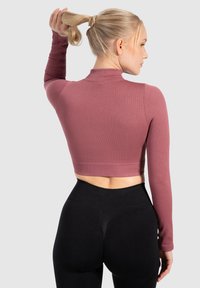Geribbelde, langmouw cropped top in mauve met een hoge hals, gecombineerd met hooggeplooide zwarte leggings, die gladde texturen en een aansluitend ontwerp tonen.