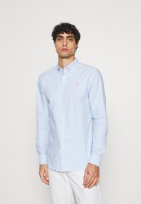 Hellblaue Langarmbluse aus strukturiertem Stoff, mit einem Button-Down-Kragen und einem kleinen gestickten Logo auf der Brust.
