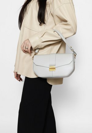 Borsa in ecopelle grigia con un design strutturato, hardware dorato e chiusura a patta, portata da una persona con un top beige.