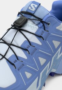 Αθλητικό παπούτσι ανοιχτού μπλε χρώματος με υφή υφάσματος, ενσωματωμένα κορδόνια και μαύρες λεπτομέρειες. Διαθέτει καλουπωμένη σόλα και χαρακτηριστικά γεωμετρικά σχέδια.