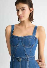 Denimkleid mit quadratischem Ausschnitt, breiten Trägern und tailliertem Oberteil. Es hat eine taillierte Taille und dezente Nähte in einem mittleren Blauton.
