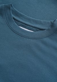 Türkise Baumwoll-T-Shirts mit Rundhalsausschnitt, die eine glatte Stofftextur und Nähdetails entlang des Kragens und Saums zeigen.