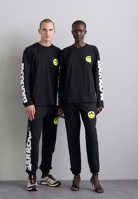 Black long-sleeve shirts and pants featuring neon smiley face accents. Brand name "BARROW" in white on sleeves. Smooth texture, casual fit.