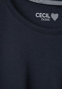 Marineblaue T-Shirt mit Rundhalsausschnitt, aus weicher Baumwolle hergestellt. Mit einem weißen "Cecil basic" Logo und einem gestreiften Innenhalsbündchen.