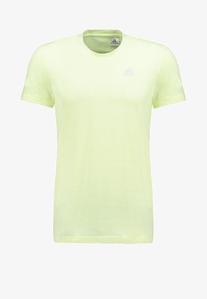T-shirt ajustée vert clair associée à un short gris et des chaussures de sport blanches. Le t-shirt est en tissu texturé et a un col rond.