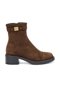 Stivale alla caviglia in suede marrone con punta arrotondata, zip laterale e una fascia decorativa con una fibbia dorata. Tacco piatto nero.