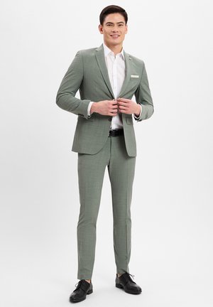 Light green, textured suit with a fitted design. Paired with a white button-up shirt and black leather shoes. Notable detail: pocket square.