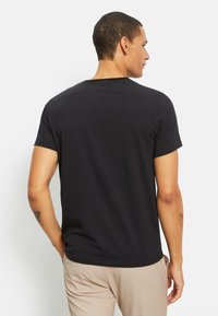 T-shirt nera a maniche corte con collo rotondo, realizzata in cotone morbido. Presenta un taglio comodo e un design semplice, con dettagli minimi.