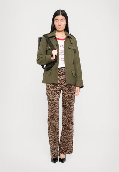 Jacket z vlněné směsi olivově zelené barvy s kapsami, bílý tričko s grafikou, leopardí puntíkované kalhoty se širokými nohavicemi a černé lodičky se špičatou špičkou.