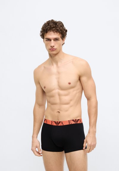 Boxer neri con fascia in vita rossa con il logo. Il tessuto è liscio e aderente, con un design minimalista.