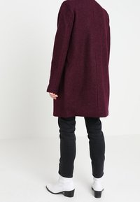 Abrigo de lana burdeos con mangas largas y corte recto, combinado con vaqueros negros y botines blancos. Diseño sencillo, sin patrón visible.