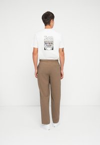 White cotton t-shirt with colorful Crayola crayon design on the back, paired with loose-fitting brown textured trousers and white sneakers.