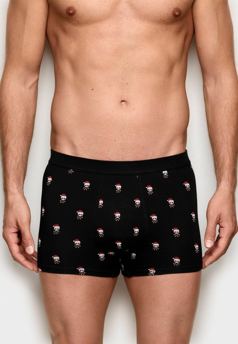 Sorte boksertrusser lavet af blødt stof med et mønster af små kranier, der bærer julesokker og slikstænger.