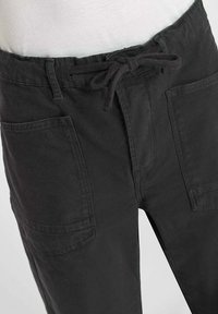 Zwarte cargobroek met een trekkoord in de taille, twee voorklauwen en een gladde textuur. De broek heeft een relaxte pasvorm en stevige stof.