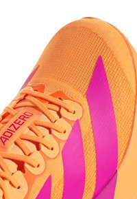 Bright orange athletic shoe with pink accents. Features textured fabric upper, flat laces, and a padded tongue. Branding on the side.