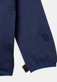 Mörkblå sweatshirtärm med texturerat tyg, försett med en logotypapplikation och detaljerade manschetter med knappar. Slät och åtsittande design.