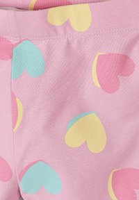 Tissu rose avec couture cousue, décoré de grandes formes de cœur pastel en jaune, bleu et rose qui se superposent.