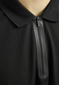 Zwarte polo met een gestructureerde stof, voorzien van een korte rits aan de voorkant, omrand door een gladde band, en een klassiek kraagontwerp.