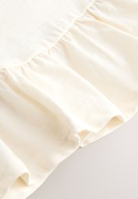 Tessuto morbido color crema con una cucitura arricciata che crea delicati volant lungo il bordo.