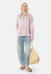 Chemisier long à manches en satin violet clair avec un motif floral, associé à un jean large déchiré bleu clair et des sandales à talons beiges.