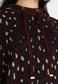 Bordeaux hoodie met zwarte luipaardprint en metallic accenten. Voorzien van een ribbelnekkraag met verstelbare trekkoorden en contrasterende hardware.