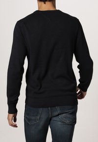 Pull bleu marine foncé en tissu tricoté, avec un col rond et des poignets côtelés. Le dos présente un détail subtil de couture en forme de V.